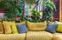 Vibrant lounge area featuring a lush indoor garden with tropical plants and a cozy, quilted yellow sofa adorned with colorful cushions.
