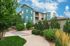 Charming modern apartment building with vibrant teal accents, nestled in lush greenery under a bright blue sky.