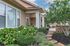 Charming front porch with lush greenery, colorful flowers, and a stone pathway leading to a cozy seating area.