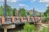 Scenic brick and steel bridge over a tranquil river, surrounded by lush greenery and picturesque mountain views.