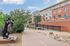 Charming apartment complex exterior with a distinctive brick facade, lush greenery, and a unique sculpture, offering a serene and inviting atmosphere.