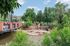 Charming riverside park scene with a vibrant brick bridge, lush greenery, and playful slide, perfect for outdoor relaxation and family fun.