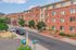 Charming urban apartment complex with red brick facade, vibrant trees, and convenient street parking, set in a scenic neighborhood.