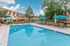Inviting swimming pool area surrounded by lush greenery and modern apartment buildings, complete with stylish lounge chairs and vibrant umbrellas for a perfect relaxation spot.