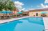 Inviting apartment community pool area with bright blue umbrellas, comfortable lounge chairs, and lush greenery set against a clear sky.