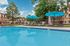 Inviting outdoor pool area with vibrant blue umbrellas and comfortable loungers, set against lush landscaping and a charming apartment backdrop.