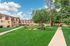 Charming apartment complex surrounded by lush green lawns and mature trees under a clear blue sky.