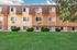 Charming apartment building with modern architecture, featuring lush green lawn and vibrant vegetation, basking under a bright blue sky.