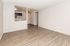 Bright living space with sleek wood flooring, modern open-plan access to kitchen featuring dark cabinets, and a ceiling fan for comfort.