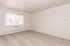 Bright, spacious room with plush carpet, large window with vertical blinds, and built-in air conditioning unit.