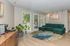 Bright living room featuring a stylish green sectional sofa, large windows with lush outdoor views, and a vibrant circular rug on light wood flooring.