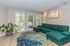 Bright, modern living room with a stylish green sectional sofa, vibrant area rug, and large windows leading to a patio, perfect for entertaining and relaxation.