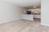 Modern open-concept living space with plush carpet and a sleek kitchen featuring white cabinetry and black appliances.