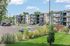 Contemporary apartment complex with modern balconies, vibrant landscaping, and ample parking under a clear sky.