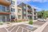 Modern apartment complex with three stories, each featuring private balconies, surrounded by lush greenery and a well-maintained parking area.