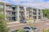 Modern apartment complex with spacious balconies and ample parking, surrounded by lush greenery and clear skies.