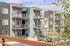 Modern apartment building with stylish balconies, surrounded by greenery and sunny skies.