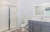 Modern bathroom with sleek grey cabinetry, illuminated mirror, and spacious glass-enclosed shower.