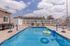 Inviting outdoor swimming pool with volleyball net, surrounded by lounge chairs and vibrant floaties, under a sunny sky.