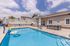 Inviting pool area with sun loungers and a modern patio, set against a backdrop of a charming clubhouse, perfect for relaxation and entertainment.