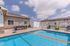 Charming outdoor pool area with volleyball net, surrounded by a cozy patio and seating, under a beautiful blue sky.