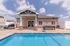 Charming poolside view of a modern home with inviting outdoor seating, perfect for sunny leisure and gatherings.
