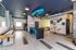 Modern communal lounge with stylish seating, vibrant decor, and a sleek kitchenette, featuring unique elements like a ceiling kayak and neon signage.