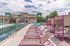 Modern apartment complex featuring a luxurious swimming pool with vibrant pink lounge chairs and shaded cabanas, offering a perfect summer retreat.
