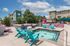 Vibrant apartment outdoor area with a cozy spa pool, colorful lounge chairs, and lush greenery under a clear sky.