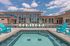 Luxurious apartment complex with an inviting swimming pool, chic poolside seating, and modern architecture under a bright sky.