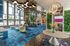 Modern and vibrant apartment lobby with striking blue carpet, unique lighting fixtures, lush green plants, and contemporary seating areas.