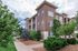 Charming apartment complex with modern architecture, surrounded by lush greenery and a welcoming pathway under a bright sky.