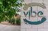 Chic apartment entrance with modern 'vibe' sign surrounded by lush greenery, offering a welcoming ambiance.