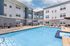 Inviting apartment complex with a refreshing swimming pool, comfortable lounge chairs, and modern barbecue area under a bright sky.