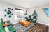 Contemporary lounge area with stylish green armchairs, geometric wall art, and a chic orange leather ottoman on a patterned rug.