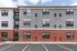 Modern apartment building with stylish brick and grey facade, featuring large windows and ample parking space.