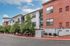 Modern apartment building exterior with stylish brick facade, large windows, and lush greenery along the street.