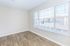 Bright, empty room with elegant wood laminate flooring and large windows offering plenty of natural light and a view of nearby apartments.