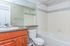 Bright, modern bathroom with elegant wooden cabinets, sleek countertop, and a pristine white bathtub.