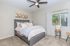 Bright and cozy bedroom featuring a plush bed with soft linens, modern ceiling fan, and large window with serene garden views.