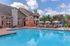 Charming apartment complex with inviting pool, sun loungers, and elegant brick architecture under a bright blue sky.