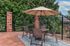 Charming outdoor patio featuring a round table with chairs and a large umbrella, set on a brick surface with lush greenery backdrop, perfect for relaxing.