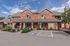 Charming brick apartment building with lush landscaping and a welcoming front entrance under a bright blue sky.