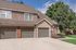 Charming townhouse with elegant stone facade, dual garages, and lush greenery, perfect for family living.