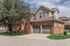 Charming townhouse with classic brick exterior and double garage, nestled in a serene neighborhood with lush green surroundings.