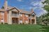 Charming two-story apartment building with rustic brick and stone exterior, featuring welcoming balconies and lush green lawns under a clear blue sky.