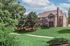 Charming brick apartment building nestled in lush greenery, featuring a spacious balcony and surrounded by a beautifully landscaped path.