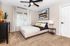 Inviting bedroom with elegant decor, featuring a cozy bed adorned with plush pillows and modern artwork above. A stylish dresser and sleek ceiling fan add a touch of sophistication.