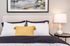 Cozy bedroom with modern decor featuring a stylish lamp and a vibrant yellow accent pillow on a neatly made bed.