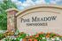 Welcome to Pine Meadow Townhomes, beautifully adorned with vibrant multicolored flowers and lush greenery set against a clear blue sky.